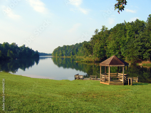 Wooden pavilion with benches chairs near large lake pond with forest trees and blue sky