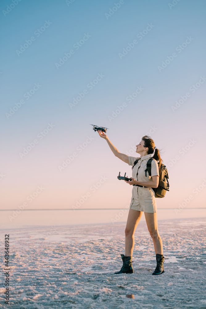 Fototapeta premium Quadcopter launch. Young woman tourist holds a drone in his hand lifting it up. Full-length side view.