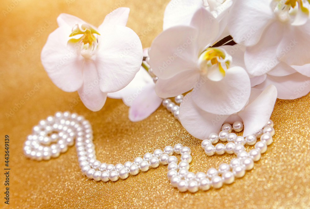 white Orchid and pearl necklace on a shiny gold background
