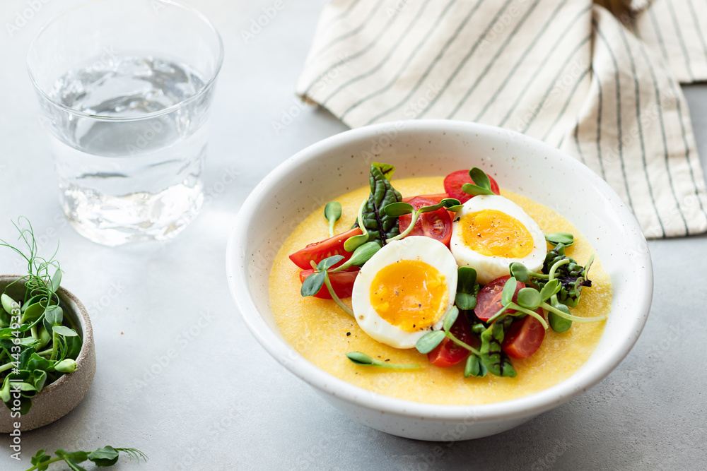 creamy polenta with eggs, fresh vegetables, microgreens on gray table. Italian cuisine concept. close-up creamy polenta with eggs, fresh vegetables, microgreens on gray table. Italian cuisine concept. close-up