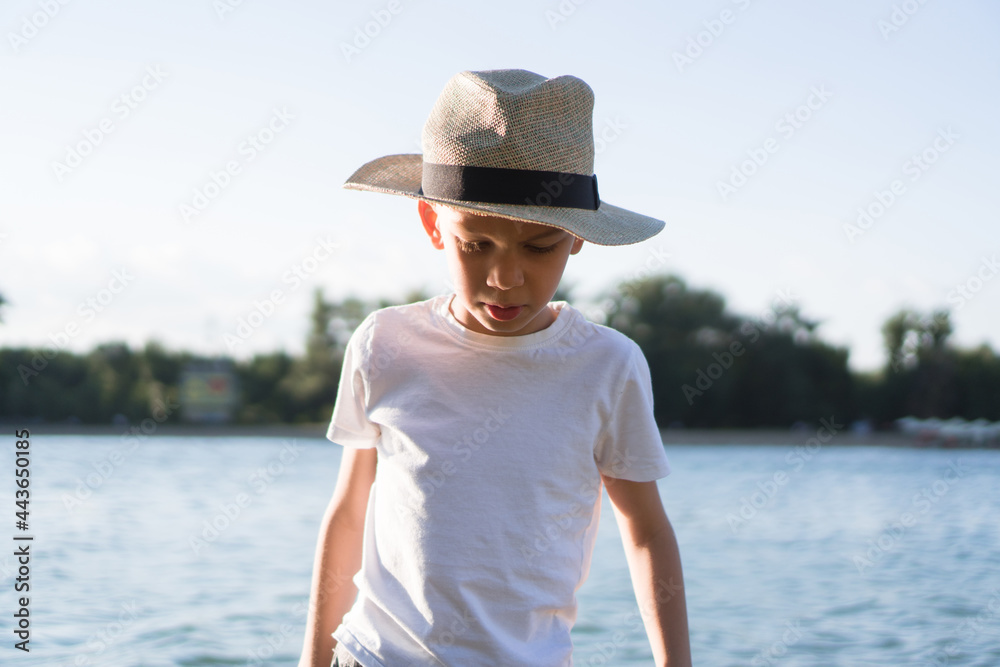 Portrait of a small boy in a hat walking by the river.