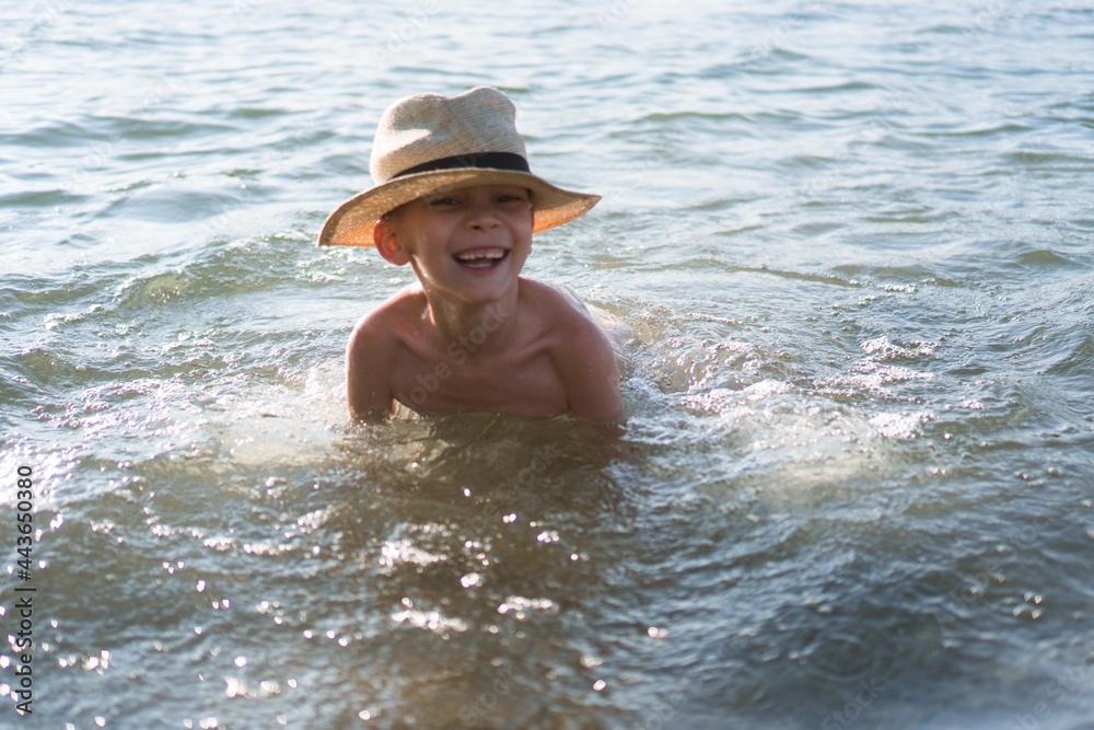 A young boy wearing a sun hat is swimming in the river while Sun goes down.