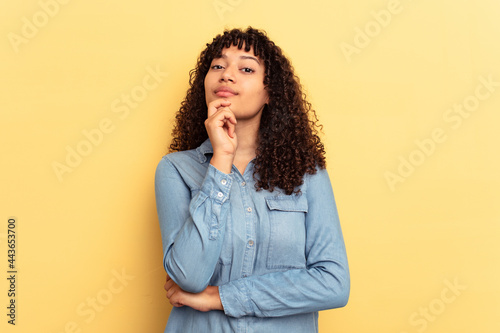 Young mixed race woman isolated on yellow background suspicious, uncertain, examining you.