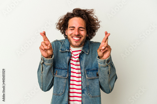 Young caucasian man isolated on white background crossing fingers for having luck photo