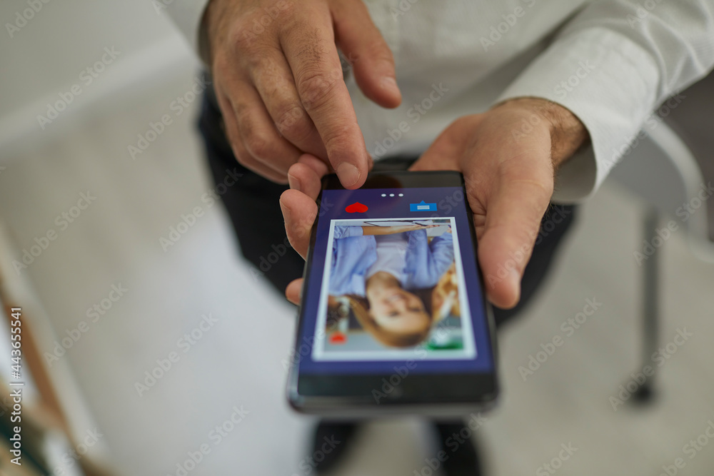 Close up of a man's hand using a smartphone to flip through women's profiles and press a heart button with his finger. Concept of finding love online and dating sites or applications. Selective focus.