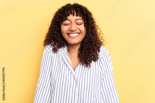 Young mixed race woman isolated on yellow background laughs and closes eyes, feels relaxed and happy.