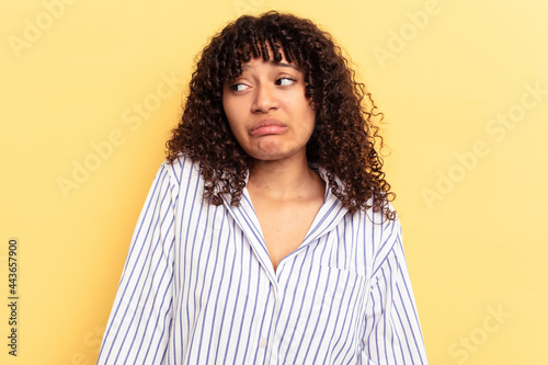 Young mixed race woman isolated on yellow background shrugs shoulders and open eyes confused.