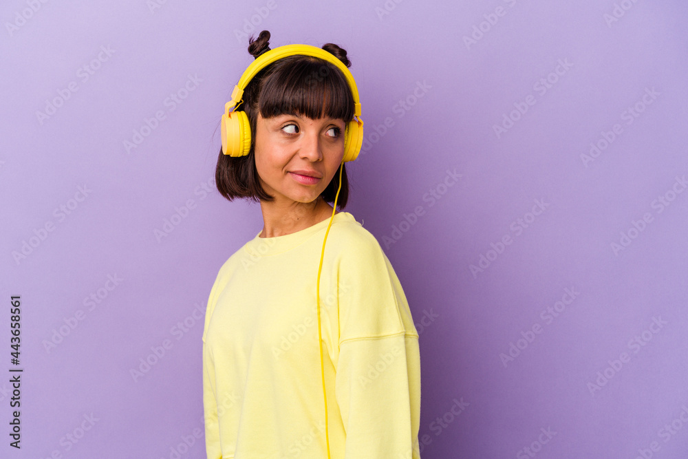 Fototapeta premium Young mixed race woman listening to music isolated on purple background looks aside smiling, cheerful and pleasant.