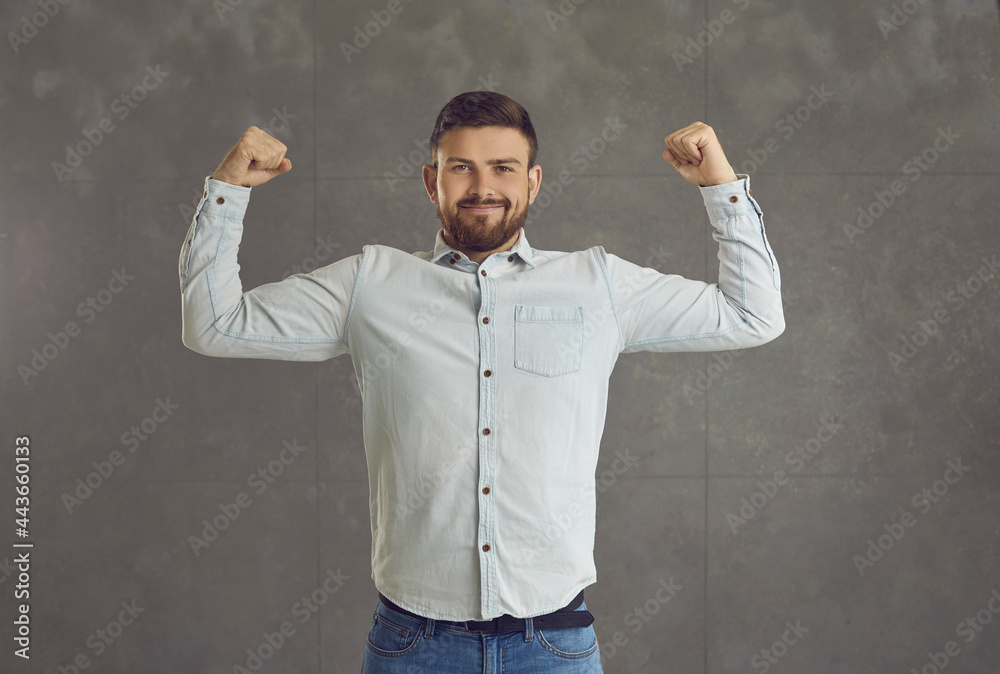 Confident satisfied handsome caucasian man office worker, ceo or businessman showing strong double biceps muscle looking at camera standing over grey studio background. Successful business concept