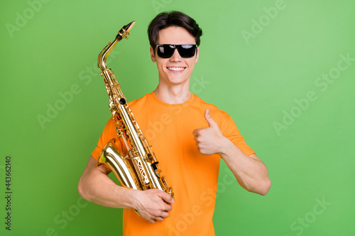 Obraz na plátně Photo of positive happy young man make thumb up wear sunlgass hold hand sax isol