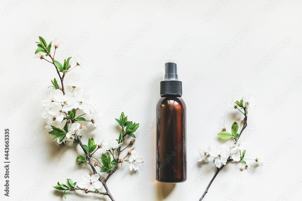 Cosmetic bottles made of dark amber glass on a white background with flowering branches of cherry or apple trees. Close-up, copy space. Beauty blogs, the concept of salon treatment, the layout of the Cosmetic bottles made of dark amber glass on a white background with flowering branches of cherry or apple trees. Close-up, copy space. Beauty blogs, the concept of salon treatment, the layout of the