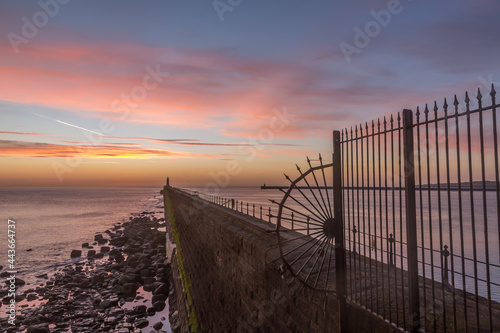 Tynemouth Pier and the Lighthouse through the metal railings with a beautiful vibrant sunrise