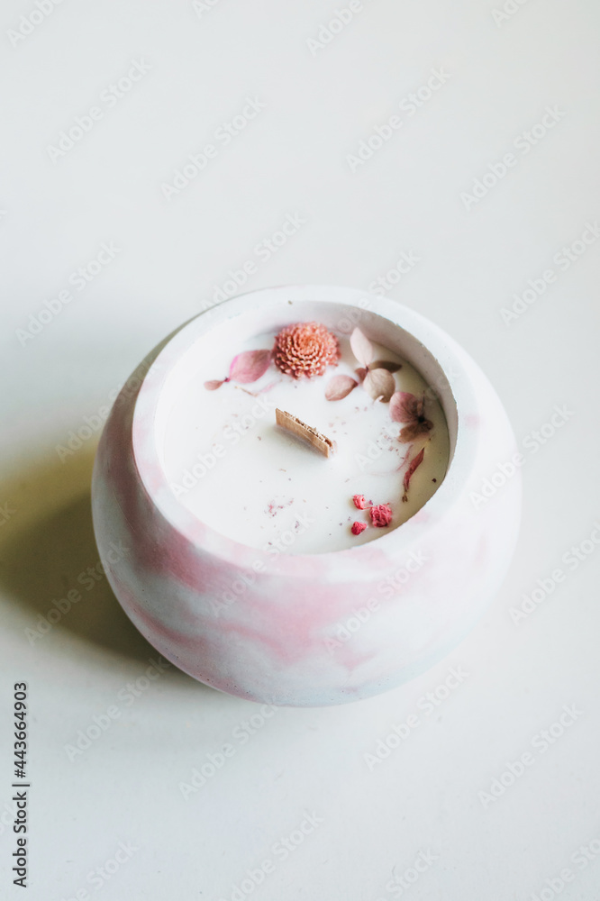 Ecological and vegan handmade candle on a white background with dry flowers in a glass made of concrete. Soy or coconut candle with a wooden wick..