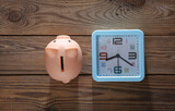 Alarm clock with piggy bank on wooden background. Top view