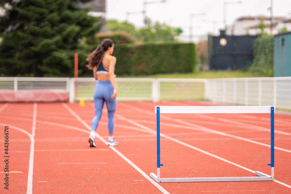 Sportswoman working out on track with hurdle Sportswoman working out on track with hurdle