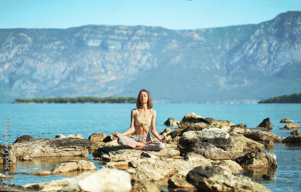 Woman yoga in nature with beautiful mountains landscape, girl sitting on stones in Lotus pose