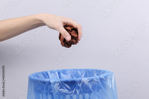 Hand throws crumpled ball of paper into trash bin with package on gray background