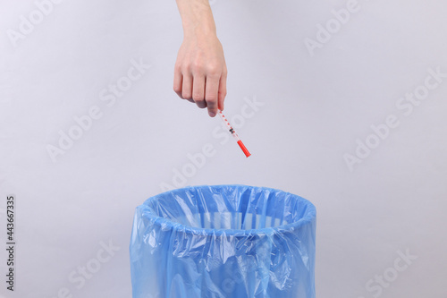 Hand throws syringe into trash bin with package on gray background photo