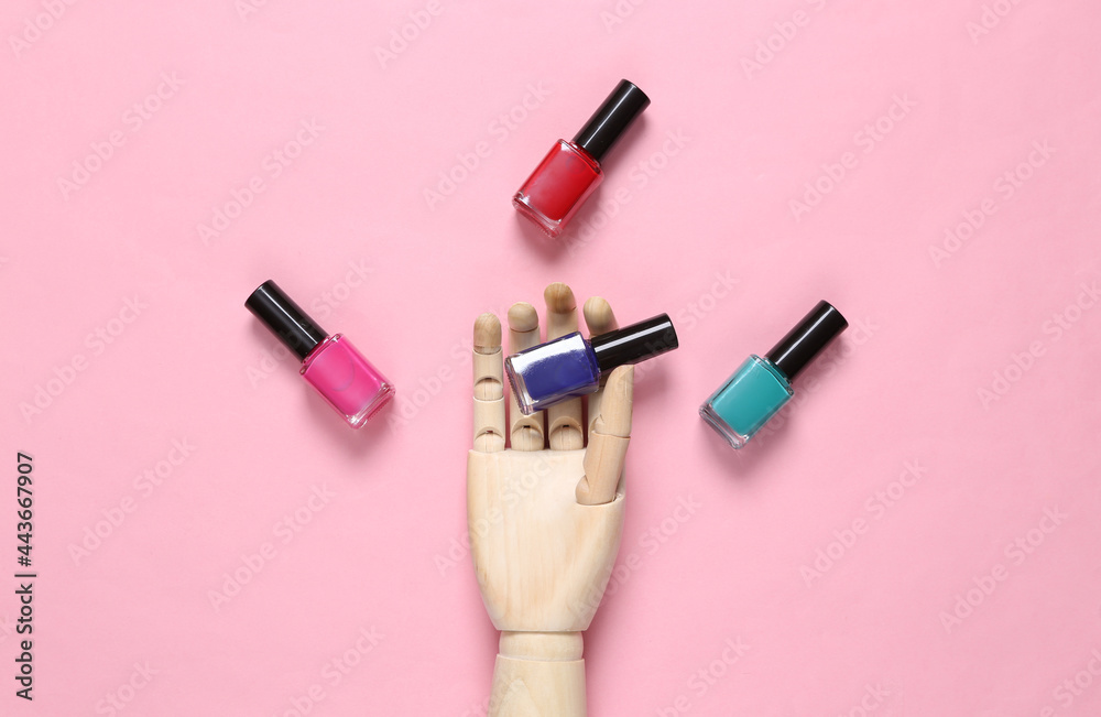 Obraz premium Wooden hand holding nail polish bottles on pink background