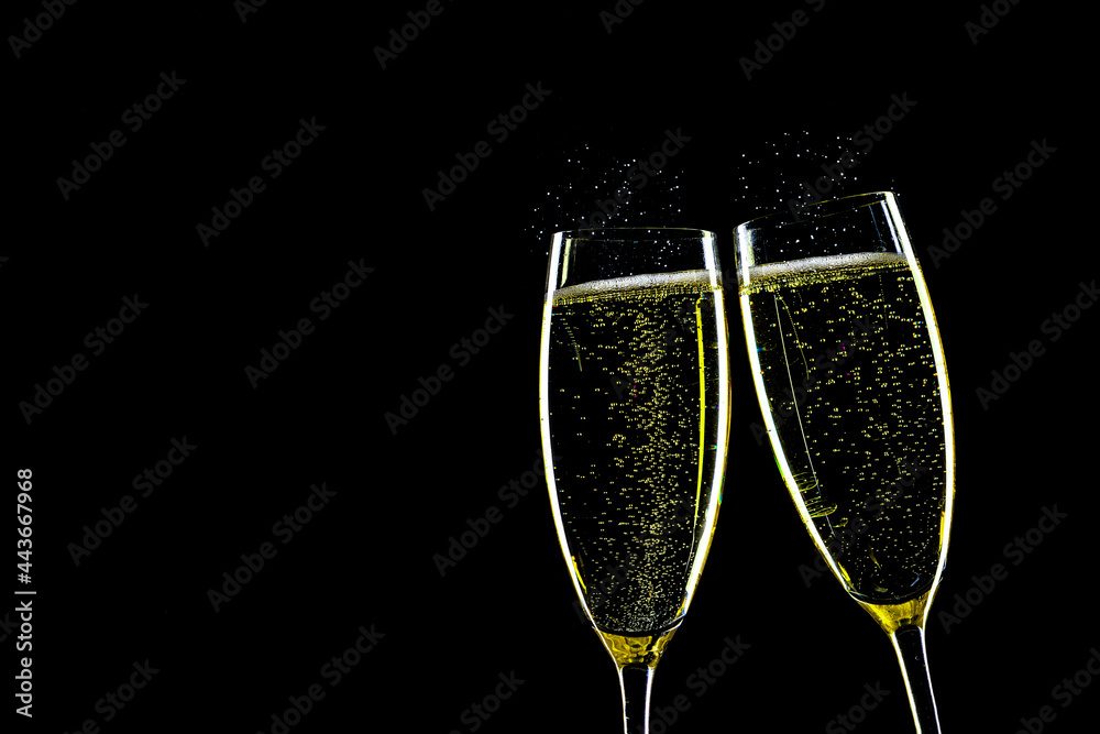 Two glasses of champagne with splashes backlit against a black