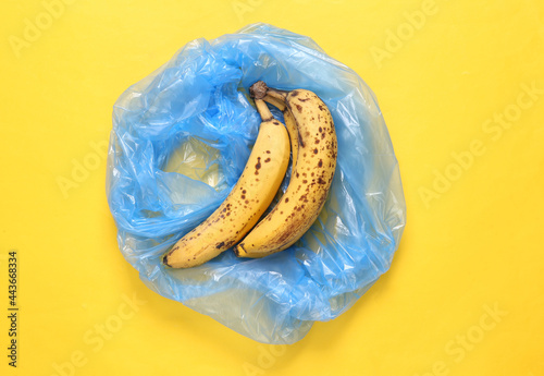 Trash packege with spoiled bananas on yellow background photo
