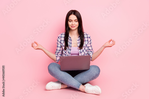 Portrait of attractive dreamy focused girl sitting lotus pose meditating using laptop isolated over pink pastel color background