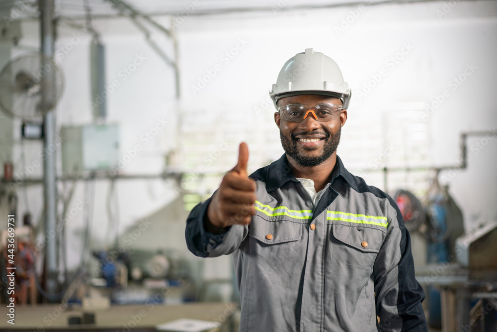 Portrait of African American male engineer in uniform smiling and showing thumbs up at industrial factory Portrait of African American male engineer in uniform smiling and showing thumbs up at industrial factory