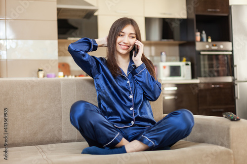 Canvastavla Young smiling woman in nightie talking on smartphone while sitting on sofa in li