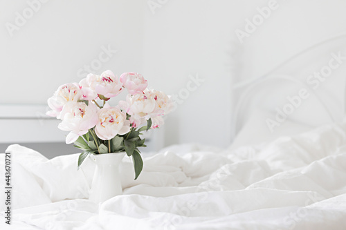 Bouquet of pink peonies on white bed linen. Modern interior in the bedroom. Wedding and festive style. © Kotkoa