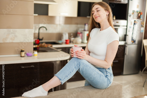 Cute young woman with a cup of coffee or tea in living room