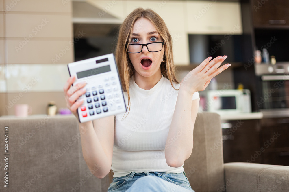 Surprised woman showing calculator while sitting on sofa in living room
