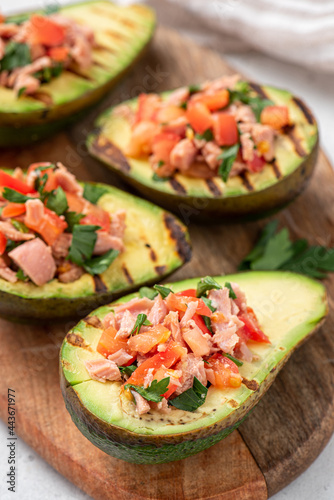 Grilled avocado stuffed with tuna, tomatoes, parsley, and olive oil on a cutting board. 