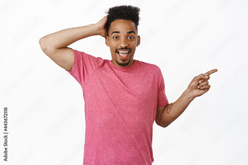 Portrait of handsome african american man in pink t-shirt, touch head and look surprised, pointing finger right at sale logo, showing banner, white background Portrait of handsome african american man in pink t-shirt, touch head and look surprised, pointing finger right at sale logo, showing banner, white background