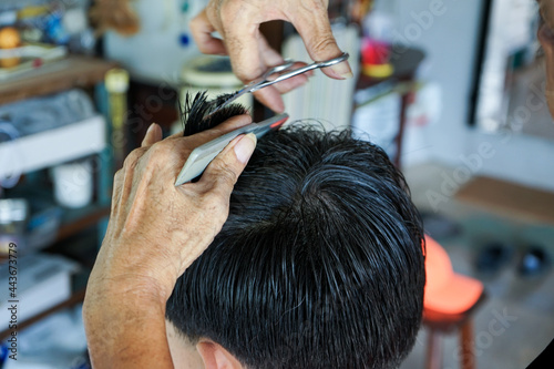 Closeup hands of hairsltylist and rear view of man having a hair cut by scissors and comb. © Phichat