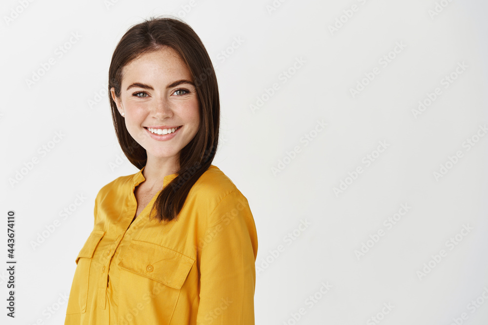 Image of young confident female manager smiling at camera, standing near copy space for company logo, white background Image of young confident female manager smiling at camera, standing near copy space for company logo, white background