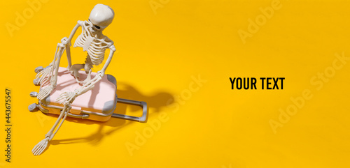 Toy skeleton with travel luggage suitcase on yellow bright background. Travel concept. Copy space