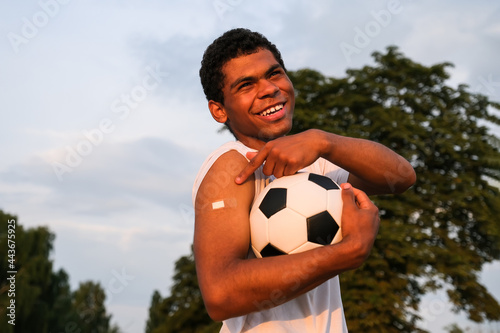 Young Afro American sportsman showing his arm after receiving vaccine at sunset © Serhii