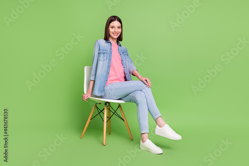 Full length photo of nice brunette hair millennial lady sit wear jeans jacket isolated on green color background