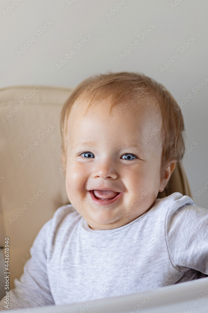 Cute caucasian infant girl ten months old sitting in baby chair and smiling on beige background. Closeup portrait of happy infant with blonde hair and blue eyes