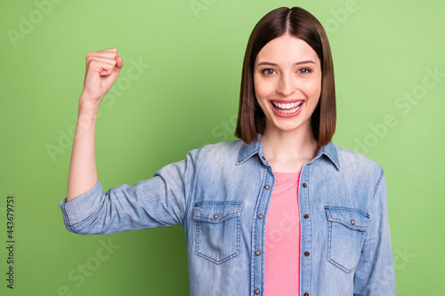 Photo of funky brunette hair young lady show biceps wear jeans jacket isolated on green color background photo