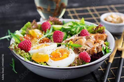 Grilled chicken meat and fresh vegetable salad of tomato, cucumber, egg, lettuce and raspberry. Ketogenic diet. Buddha bowl dish on dark background