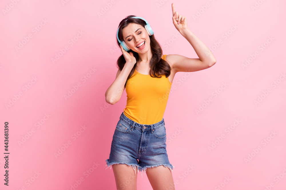 Photo of funny cute young woman wear yellow singlet listening music pointing finger isolated pink color background Photo of funny cute young woman wear yellow singlet listening music pointing finger isolated pink color background