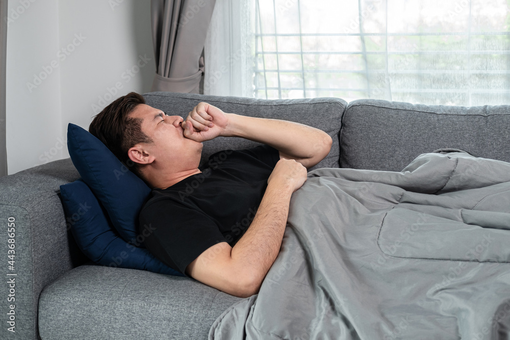 Asian man is lying with blanket on couch at home to rest when having high fever, headache and using Asian man is lying with blanket on couch at home to rest when having high fever, headache and using