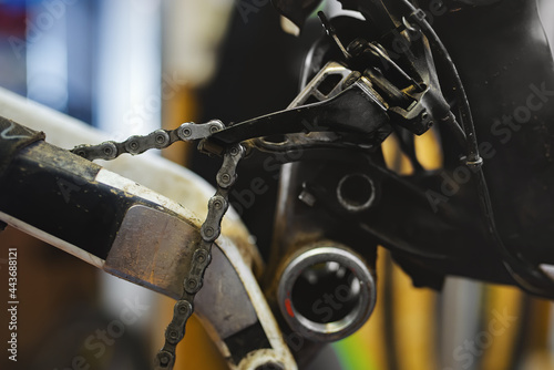 A dirty worn chain hanging in the front derailleur on a mountain bike with the bottom bracket, cranks and wheel disassembled. photo