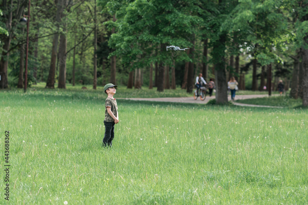 The boy runs on the green grass of the park and a drone flies over him. Boy playing with drone The boy runs on the green grass of the park and a drone flies over him. Boy playing with drone