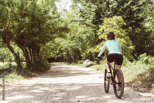 unrecognizable woman in sportswear for cyclists riding a bicycle running on a dirt road. sport life, wellness and adventure concept. copy space.