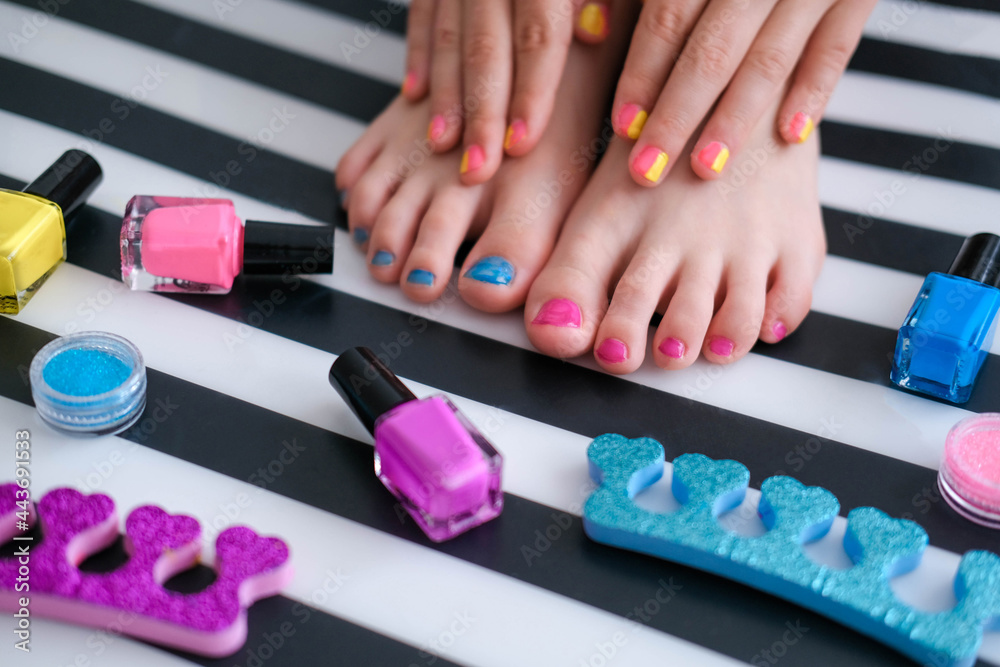 Children's feet with bright pedicure and manicure of different colors and bottles of bright nail