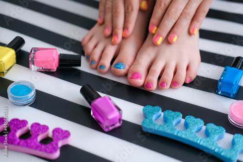 Children's feet with bright pedicure and manicure of different colors and bottles of bright nail polish. Little girl does a pedicure. Beauty salon game. Children is entertainment.