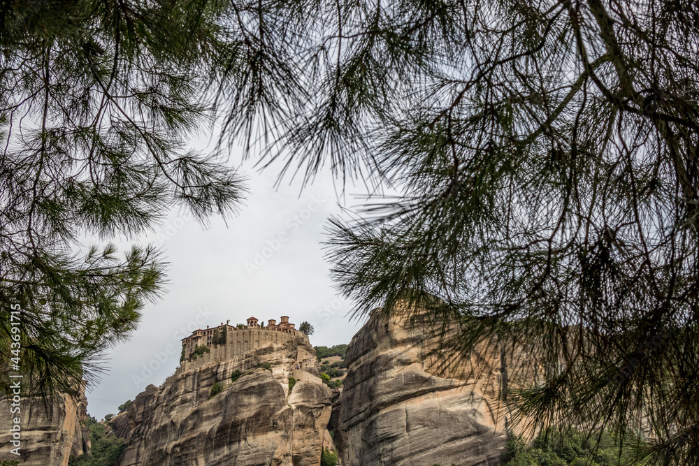 Meteora, Greece, low angle perspective of one monastery on a cliff high in the sky. Framed view by pine tree branches and needles.