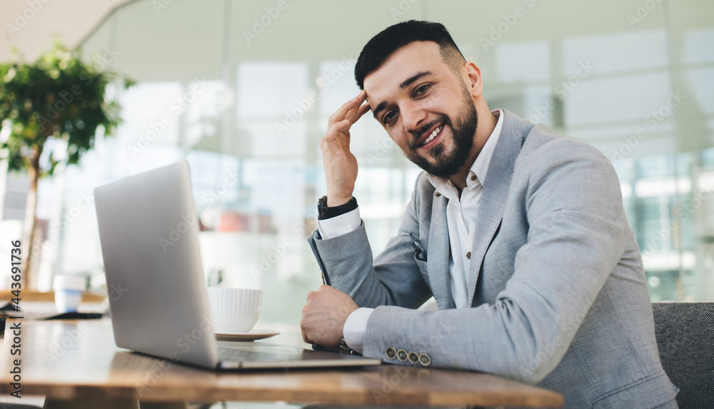 Smiling male entrepreneur working on laptop in modern workspace Smiling male entrepreneur working on laptop in modern workspace
